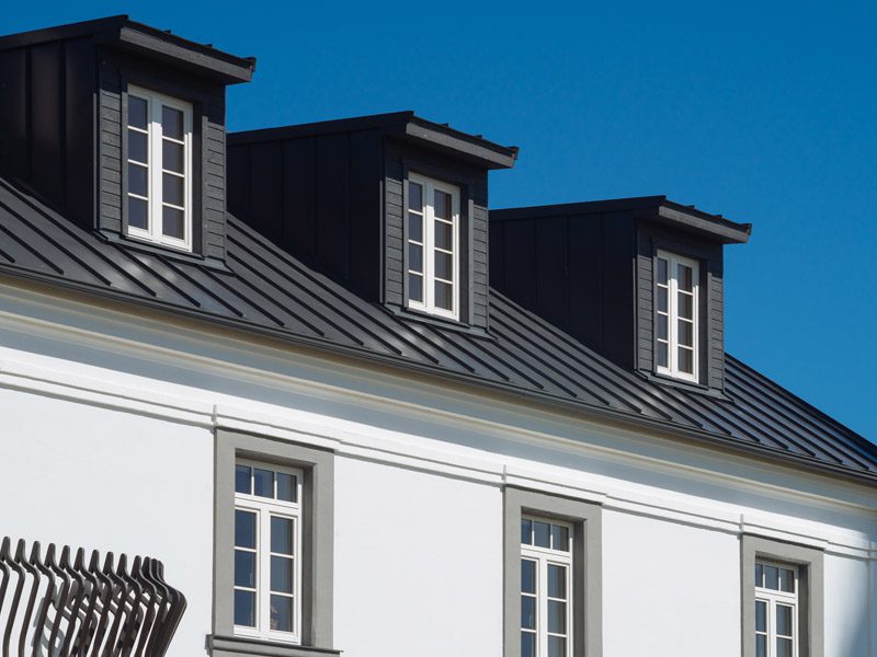 Weatherguard Roofing & Restoration | Black metal roof close up of a home with many windows where the exterior and window trim has been freshly painted