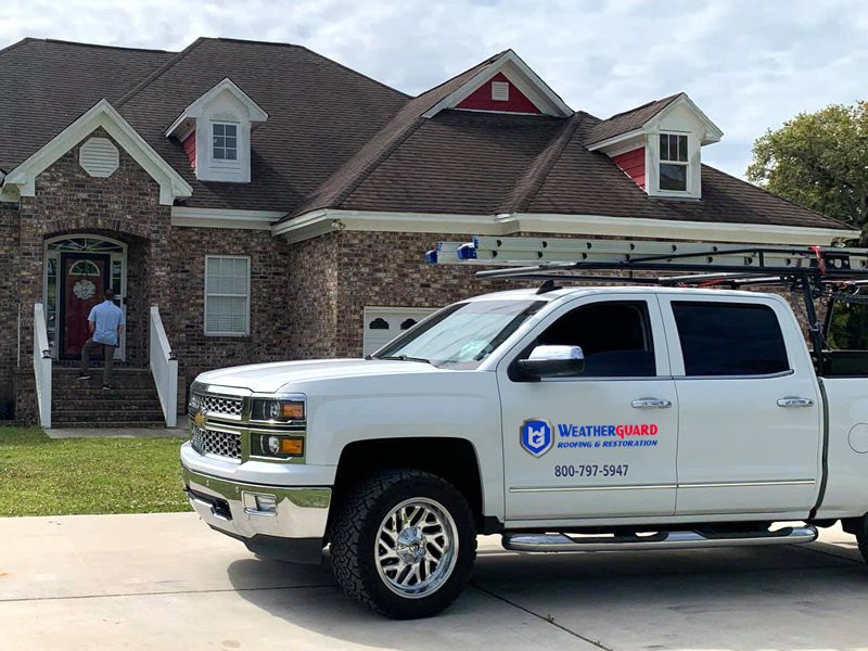 Weatherguard Roofing & Restoration | A white company truck with the Weatherguard logo and phone number parked outside of a home with new roofing just installed